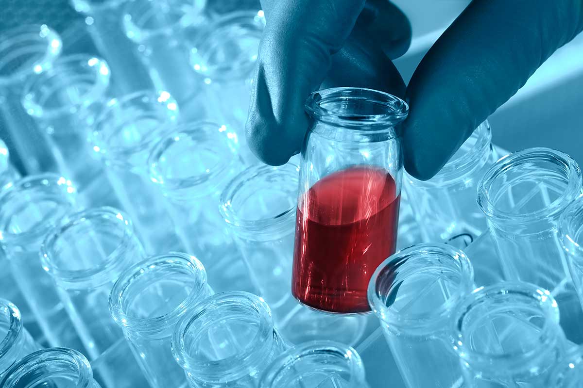 photo of gloved hand in lab with many test tubes